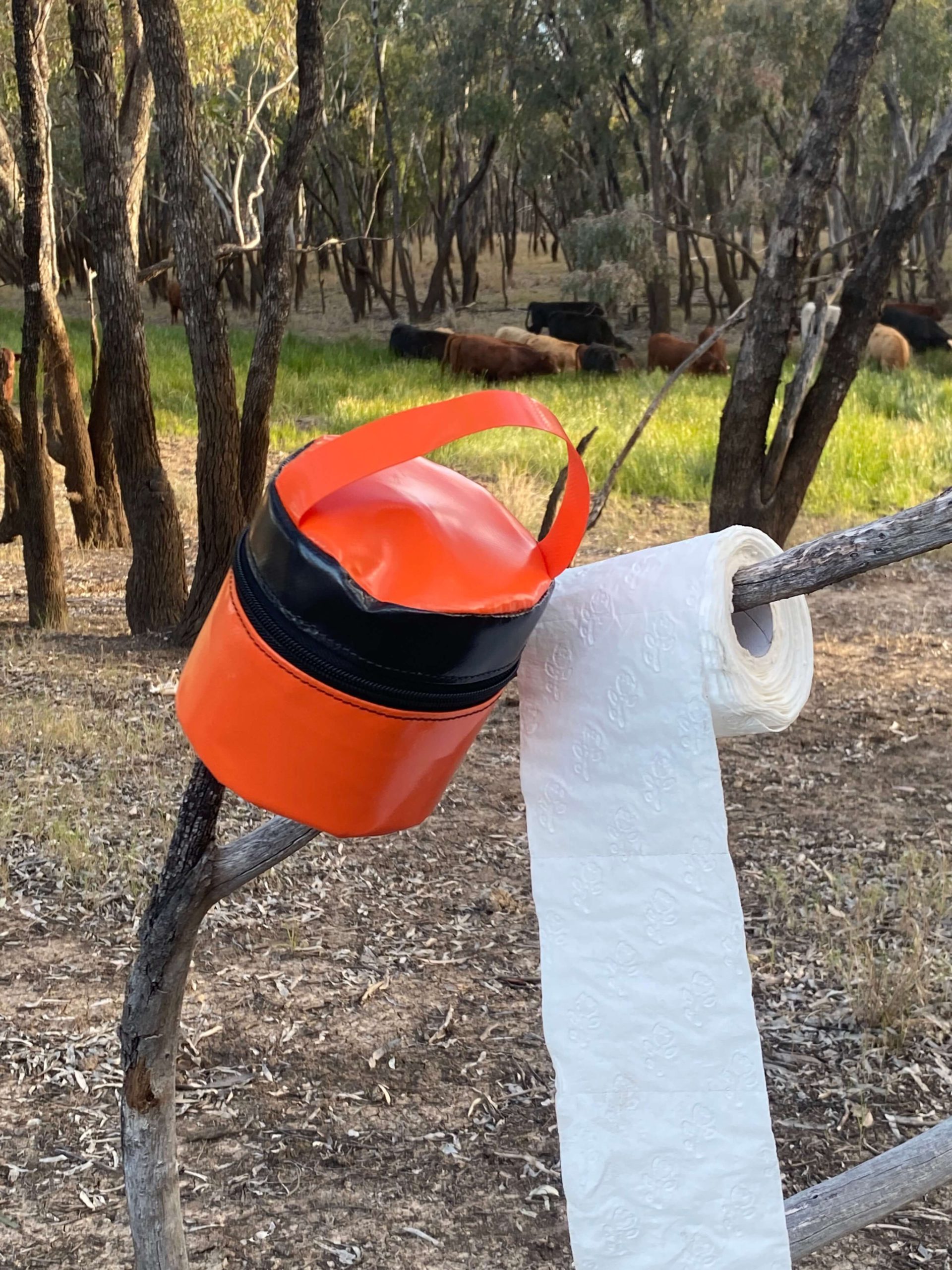 PVC toilet roll holder hanging on a tree branch with a roll of toilet paper, designed for camping and rugged outdoor use.