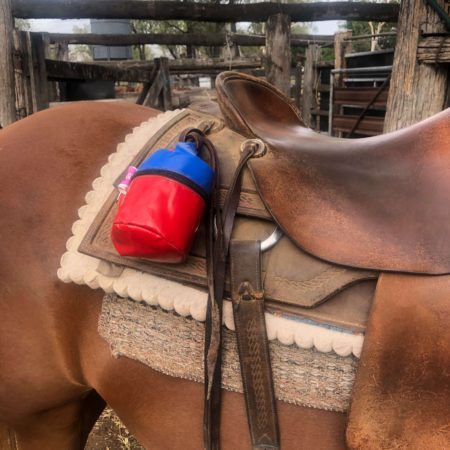 Red and blue PVC toilet roll holder secured to a horse saddle, perfect for riding, mustering, and outdoor activities.