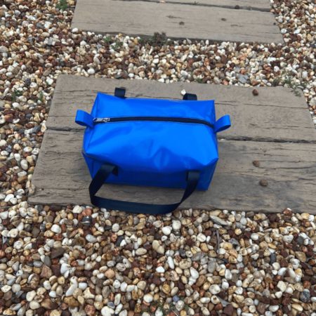 Practical Dust & Iron camping toiletry bag – water-resistant PVC design with reinforced handles, perfect for caravans and camping trips. Sitting on a pathway of rocks