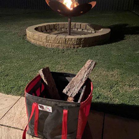 Outdoor lifestyle photo of a black and red gear bag on pavers with fire pit ambience, tough, water-resistant, and camping ready.