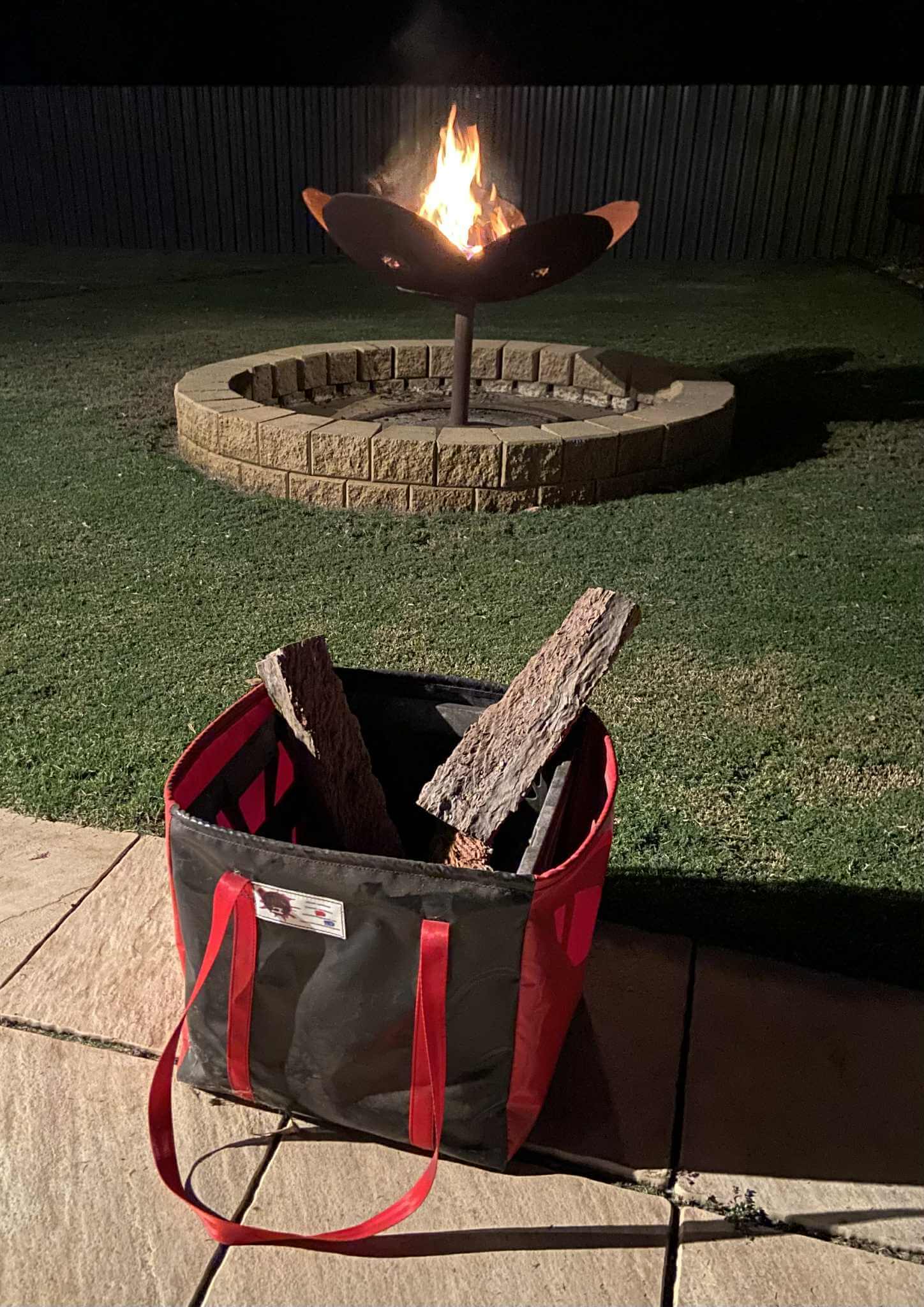 Outdoor lifestyle photo of a black and red gear bag on pavers with fire pit ambience, tough, water-resistant, and camping ready.