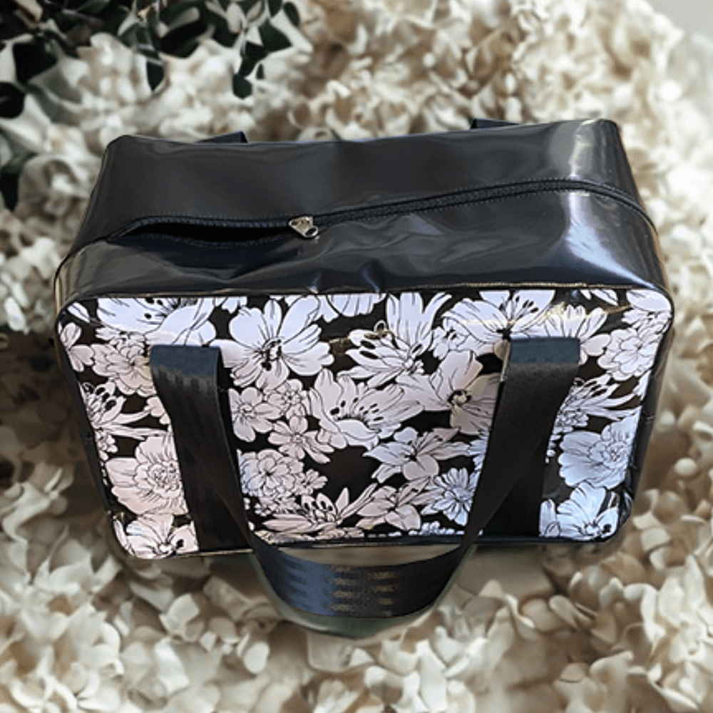 Black Weekend Gear Bag with black and white floral pattern, durable PVC vinyl, heavy-duty zip, reinforced 2-inch seatbelt webbing handles, and inside pocket – perfect for travel or sports.