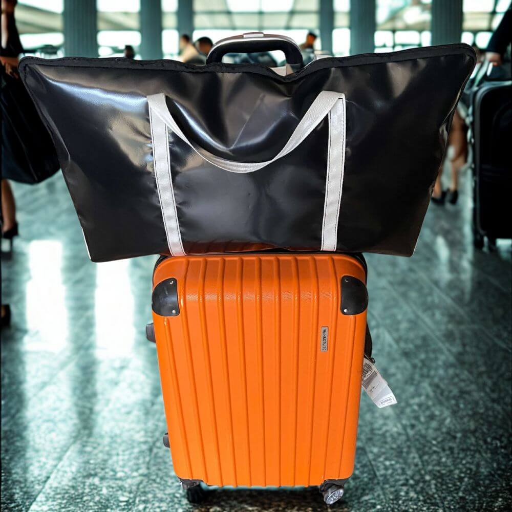 Black and white PVC pillow carry bag hanging on luggage at an airport, lightweight and protective travel accessory.