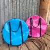 “Pink and sky blue Dust & Iron roping bag with black handles leaning against a tree with lasso rope on red dirt”