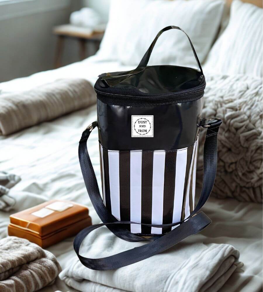 Black and white striped Shower Mate toiletry bag with shoulder strap and Dust & Iron branding displayed on a neatly made bed