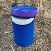 PVC Viva roll holder bag in blue and purple with a zipper opening, holding a roll of Viva hand towels, photographed outdoors near a tree.